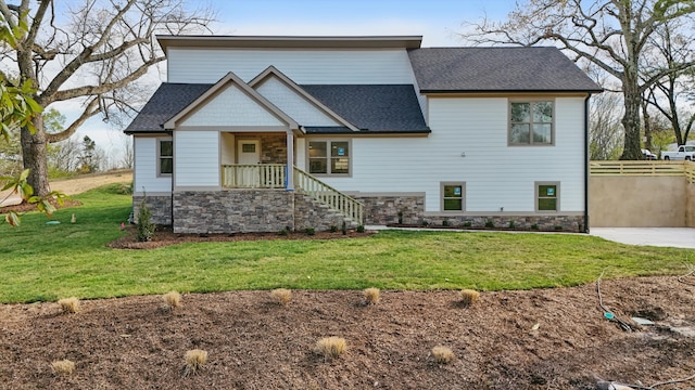 view of front of home featuring fence, a front yard, a shingled roof, and stone siding