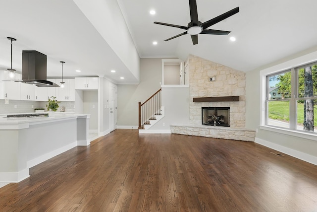 unfurnished living room with a ceiling fan, a stone fireplace, visible vents, lofted ceiling, and dark wood finished floors