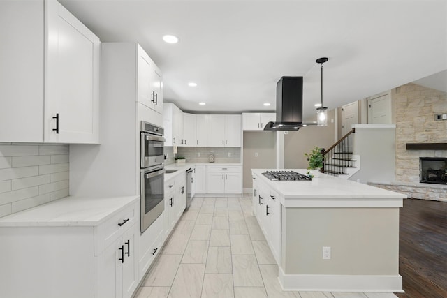 kitchen featuring island range hood, decorative backsplash, stainless steel appliances, a fireplace, and pendant lighting