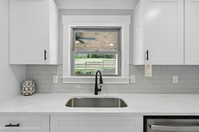 kitchen with backsplash, white cabinetry, stainless steel dishwasher, and a sink