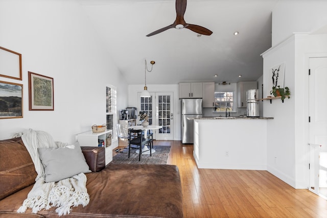 living room featuring ceiling fan, high vaulted ceiling, baseboards, and light wood-style floors