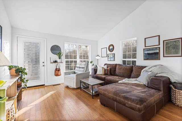 living area featuring high vaulted ceiling, wood-type flooring, visible vents, and baseboards