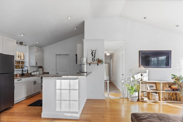 kitchen featuring light wood-style flooring, white cabinets, dark stone countertops, and freestanding refrigerator