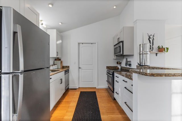 kitchen featuring lofted ceiling, light wood-style flooring, appliances with stainless steel finishes, dark stone countertops, and white cabinetry