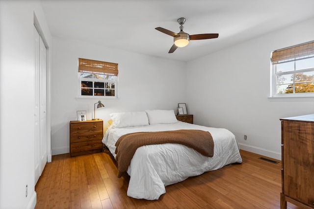 bedroom featuring hardwood / wood-style flooring, visible vents, a ceiling fan, baseboards, and a closet