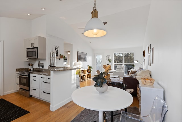 kitchen featuring dark stone counters, open floor plan, stainless steel appliances, light wood-style floors, and pendant lighting