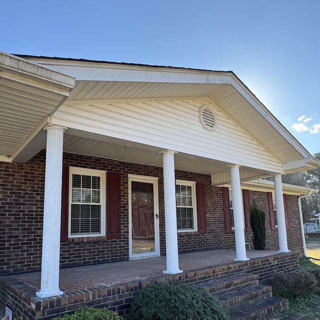 doorway to property featuring covered porch and brick siding