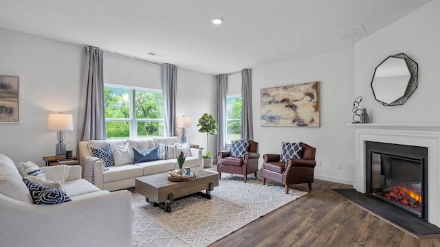 living room with wood finished floors, a glass covered fireplace, visible vents, and baseboards