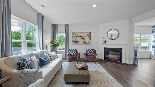 living room with baseboards, visible vents, wood finished floors, and a glass covered fireplace