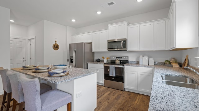 kitchen featuring visible vents, appliances with stainless steel finishes, white cabinets, a kitchen island, and a sink