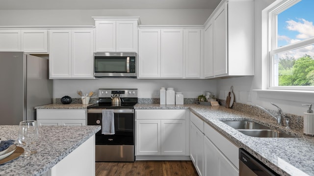 kitchen featuring light stone countertops, white cabinetry, stainless steel appliances, and a sink