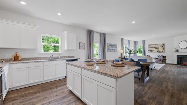 kitchen with a lit fireplace, white cabinets, a sink, and open floor plan