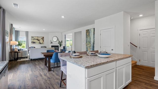 kitchen with a center island, visible vents, a glass covered fireplace, open floor plan, and white cabinets