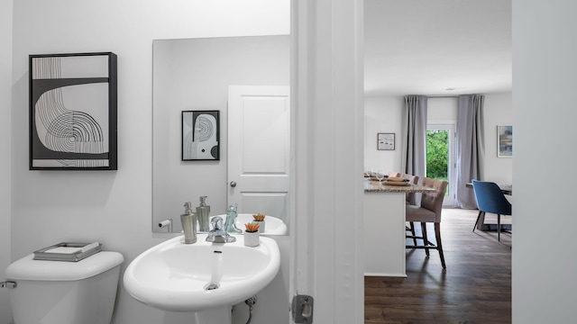 half bathroom with a sink, toilet, and wood finished floors