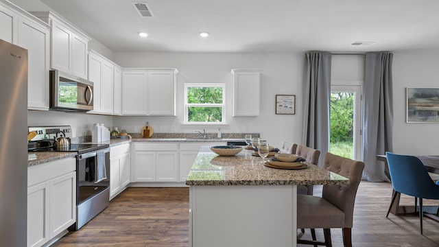 kitchen featuring light stone counters, stainless steel appliances, visible vents, white cabinetry, and a sink