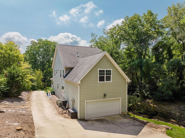 view of side of home featuring a garage, central AC, and roof with shingles