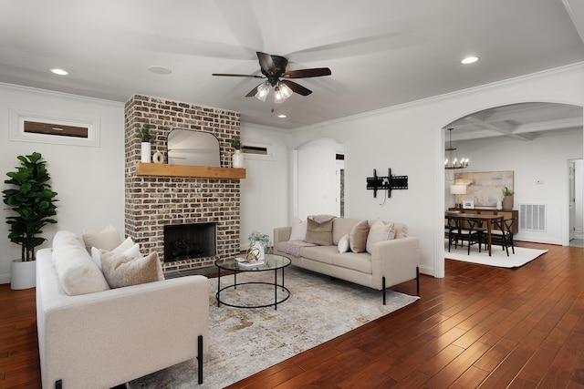 living room with arched walkways, visible vents, ornamental molding, a brick fireplace, and dark wood finished floors