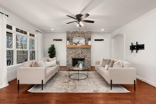 living room with ceiling fan, ornamental molding, a brick fireplace, and wood finished floors