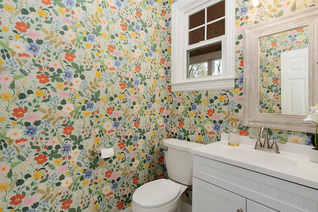 half bathroom with vanity, toilet, and wallpapered walls