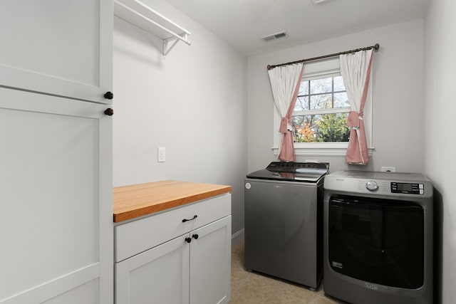 washroom with visible vents, cabinet space, and washer and clothes dryer