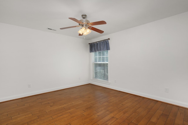 empty room featuring wood-type flooring, visible vents, ceiling fan, and baseboards