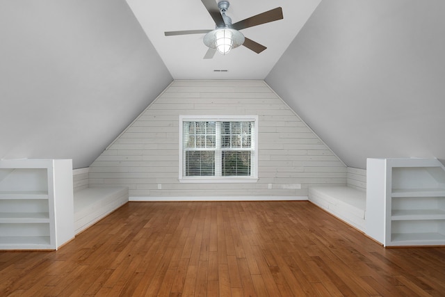 bonus room featuring built in shelves, wood-type flooring, and wooden walls