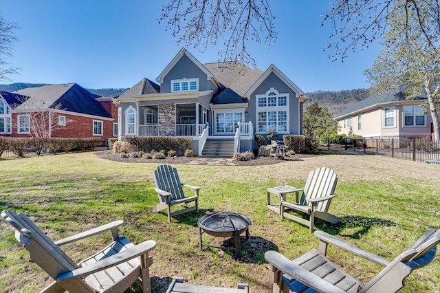 back of property featuring an outdoor fire pit, fence, a lawn, and stairs