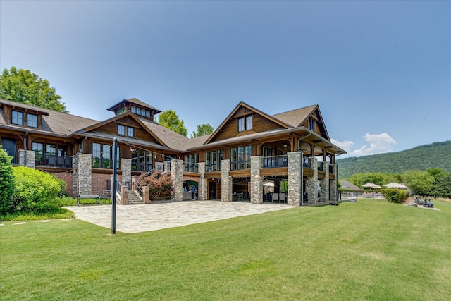 back of property with a yard, stone siding, and a patio