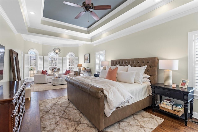 bedroom with ornamental molding, dark wood-style flooring, a raised ceiling, and recessed lighting