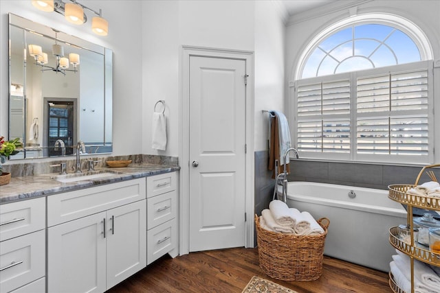 full bath with crown molding, a notable chandelier, a freestanding bath, vanity, and wood finished floors