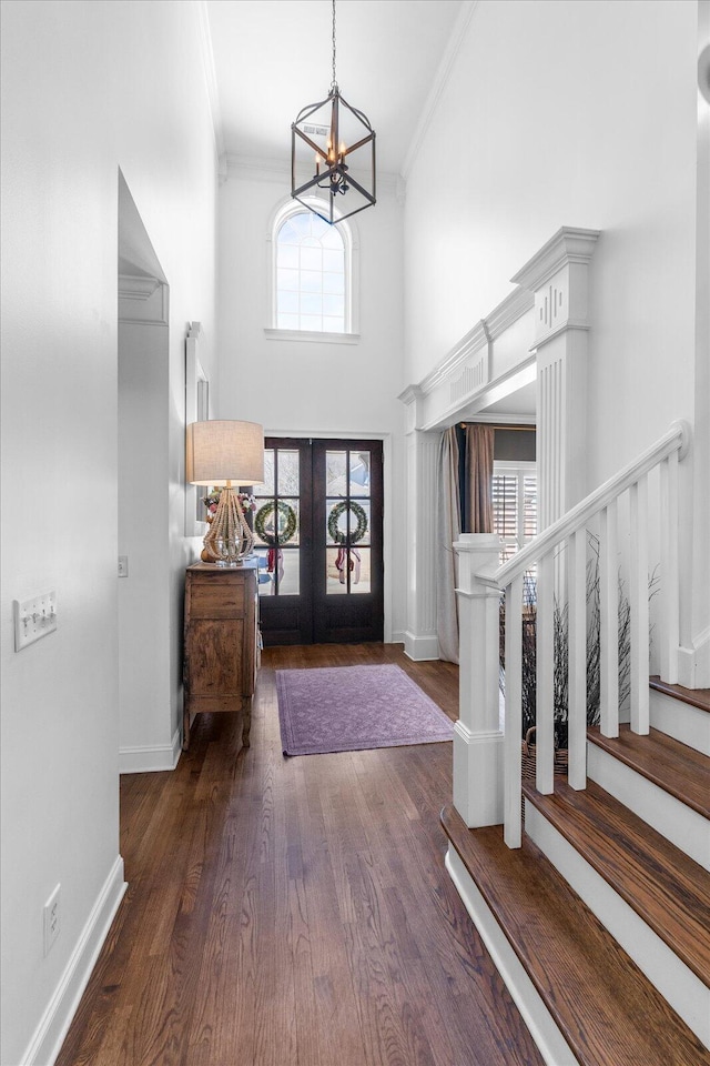 foyer featuring dark wood-type flooring, a towering ceiling, stairs, french doors, and crown molding