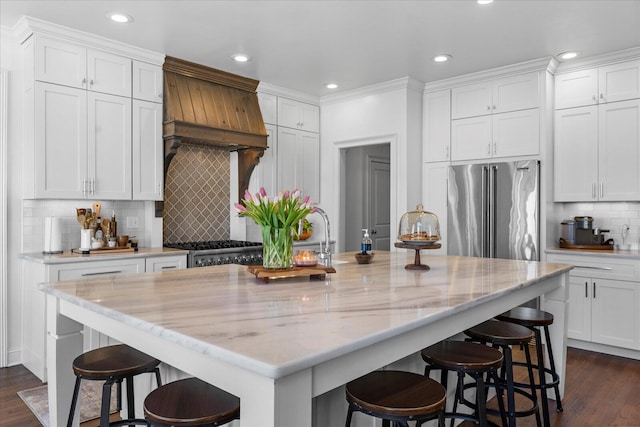 kitchen featuring light stone counters, a center island with sink, white cabinets, range, and high end refrigerator