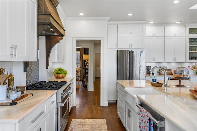 kitchen with premium appliances, a sink, white cabinets, dark wood finished floors, and glass insert cabinets