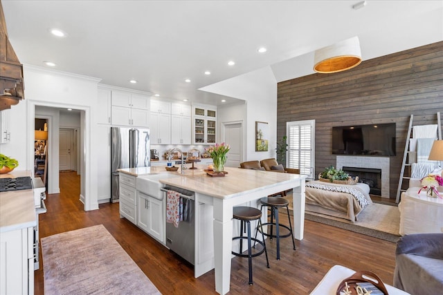 kitchen featuring appliances with stainless steel finishes, glass insert cabinets, open floor plan, a kitchen island with sink, and white cabinetry