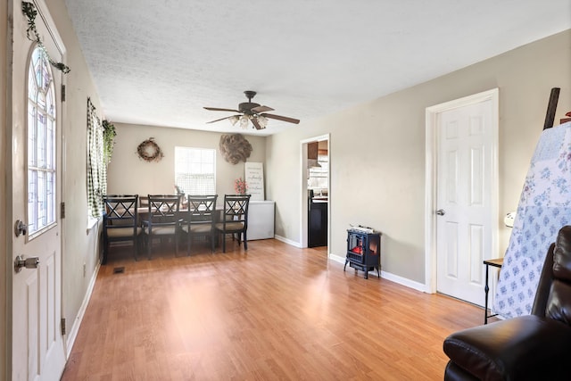 dining space featuring a wood stove, ceiling fan, a textured ceiling, light wood-type flooring, and baseboards