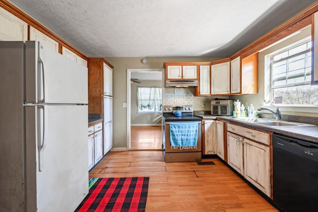 kitchen with under cabinet range hood, a sink, black dishwasher, electric stove, and freestanding refrigerator