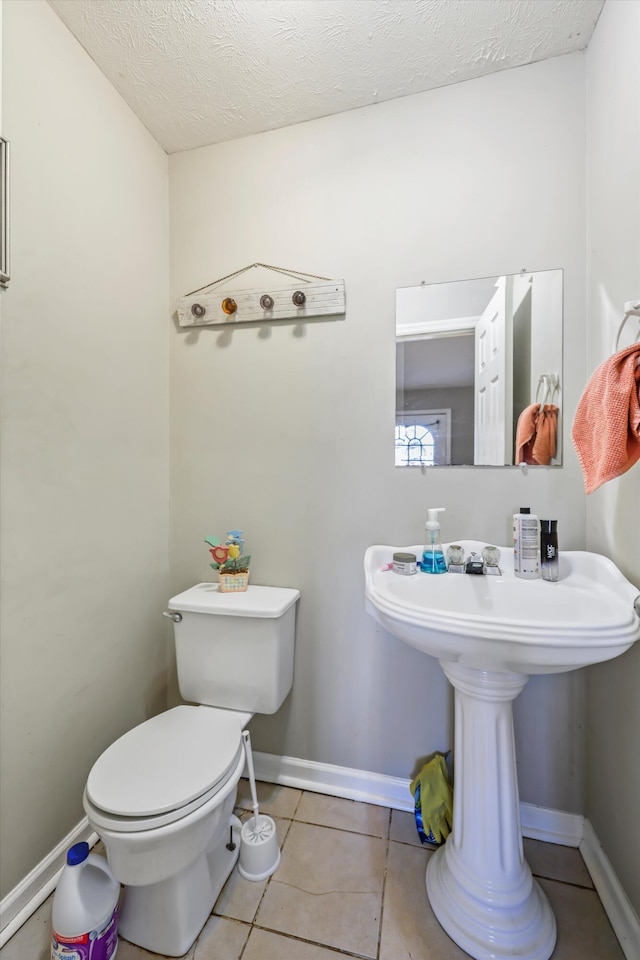 half bath with a textured ceiling, tile patterned flooring, toilet, and baseboards