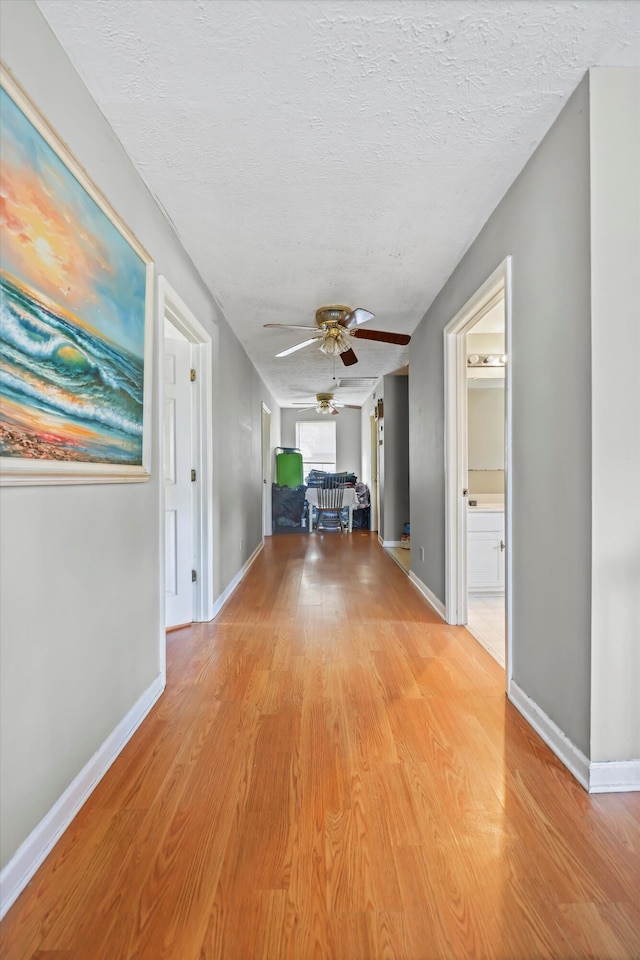 hall featuring a textured ceiling, light wood-style flooring, and baseboards