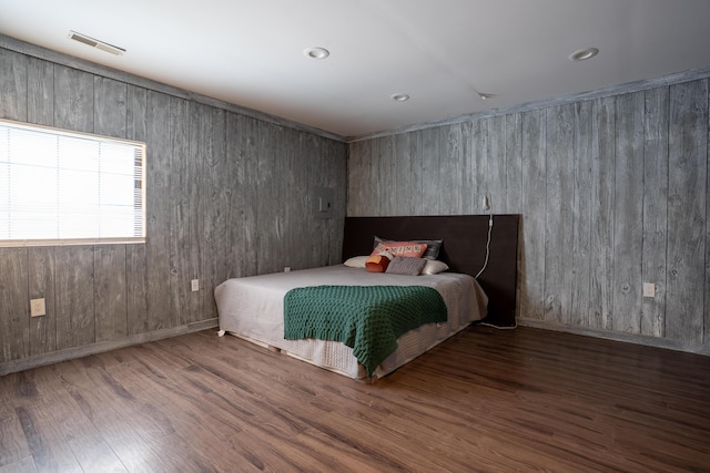 bedroom with wood walls, baseboards, visible vents, and wood finished floors