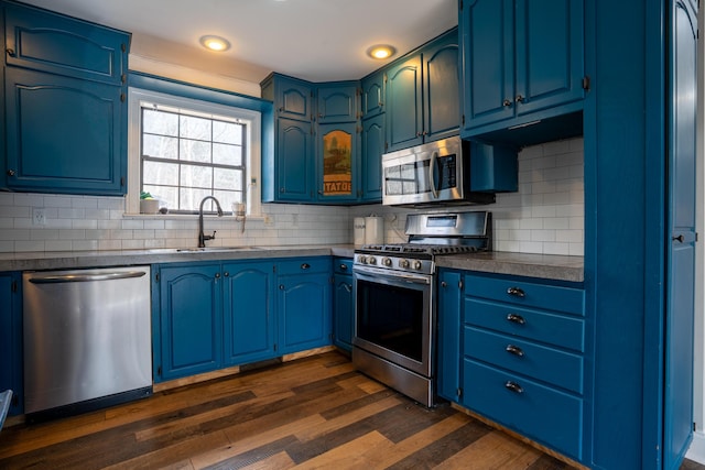 kitchen featuring tasteful backsplash, dark countertops, dark wood-style floors, stainless steel appliances, and a sink