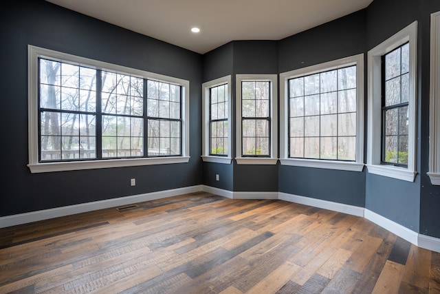 unfurnished room with wood finished floors, visible vents, and baseboards