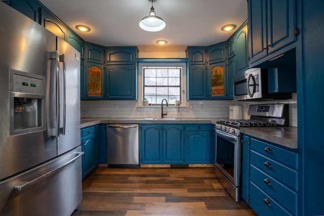 kitchen with dark countertops, appliances with stainless steel finishes, dark wood-style flooring, a sink, and backsplash