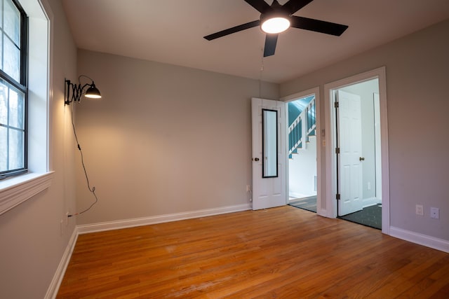 unfurnished room featuring light wood finished floors, baseboards, stairway, and ceiling fan