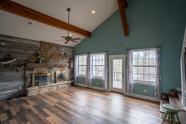 unfurnished living room with baseboards, beamed ceiling, wood finished floors, a stone fireplace, and high vaulted ceiling