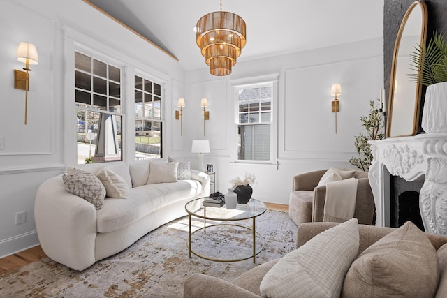 living room featuring a notable chandelier, a fireplace, lofted ceiling, wood finished floors, and baseboards