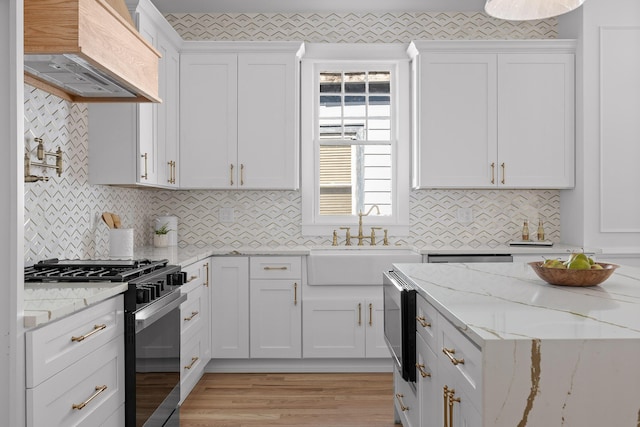 kitchen featuring white cabinets, stainless steel microwave, premium range hood, a sink, and gas stove