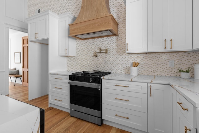 kitchen with light stone counters, premium range hood, white cabinets, black range with gas stovetop, and light wood finished floors