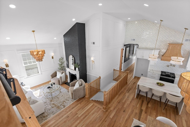 living area featuring a chandelier, a decorative wall, a fireplace, light wood-style floors, and vaulted ceiling