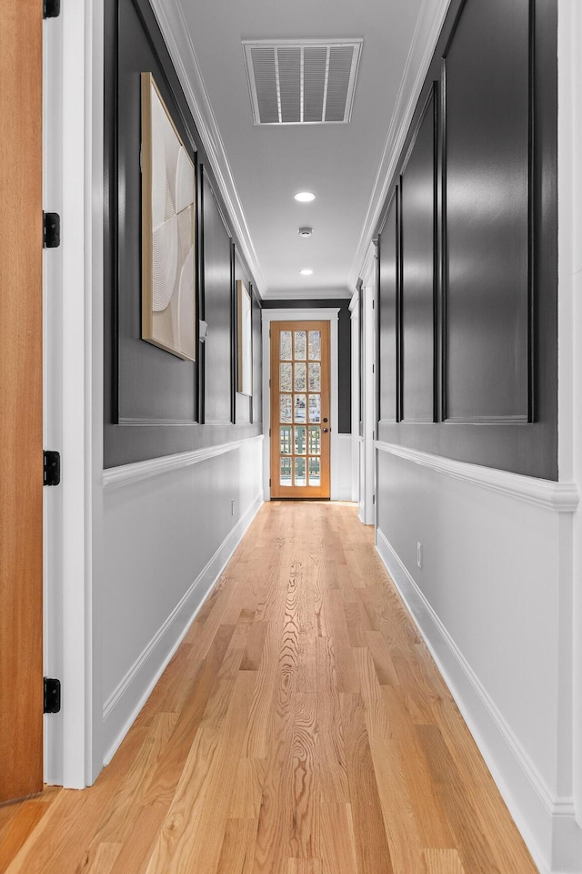 hall featuring light wood-style flooring, visible vents, baseboards, and ornamental molding