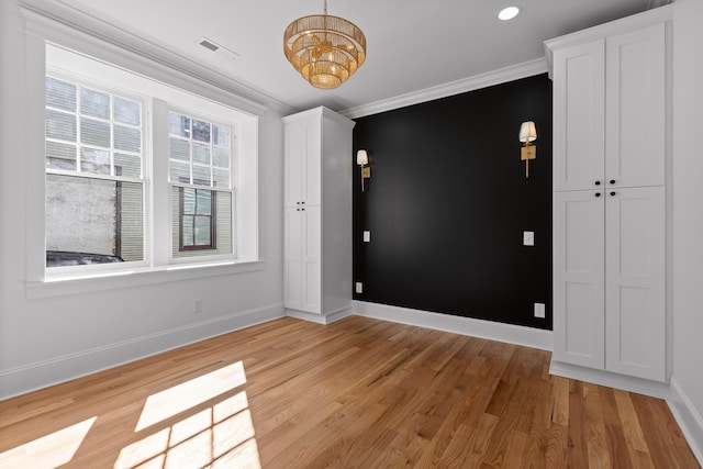 spare room featuring light wood-style flooring, visible vents, ornamental molding, and baseboards